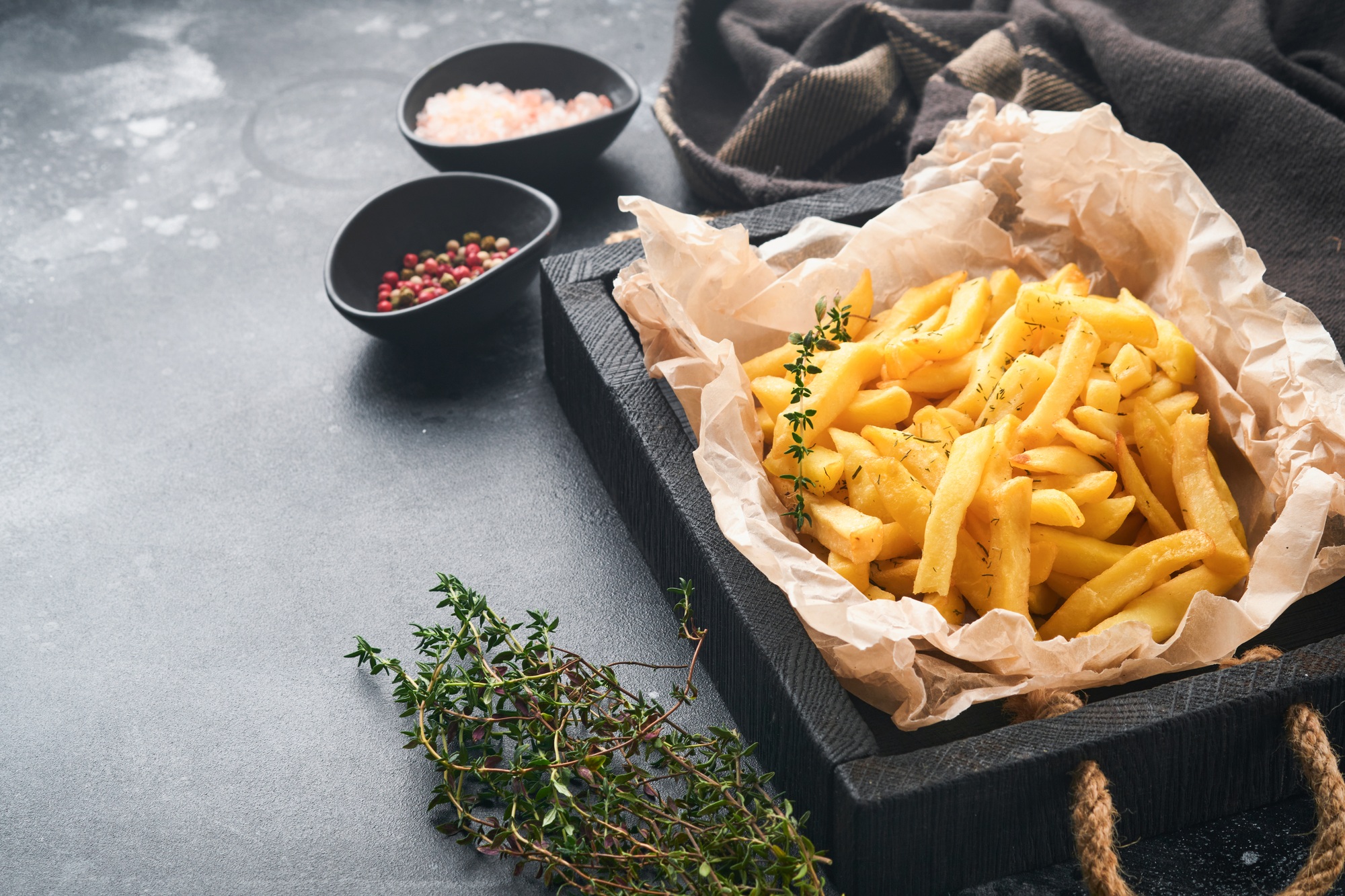 French fries. Tasty French fries server on parchment paper on wooden cutting board with tomato and c