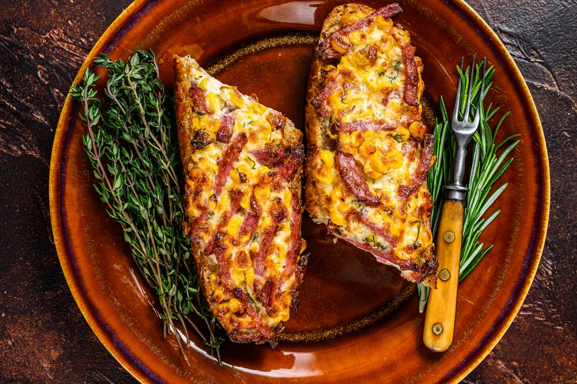 Hot baked sandwich on Baguette bread with ham, bacon, vegetables and cheese on a rustic plate.